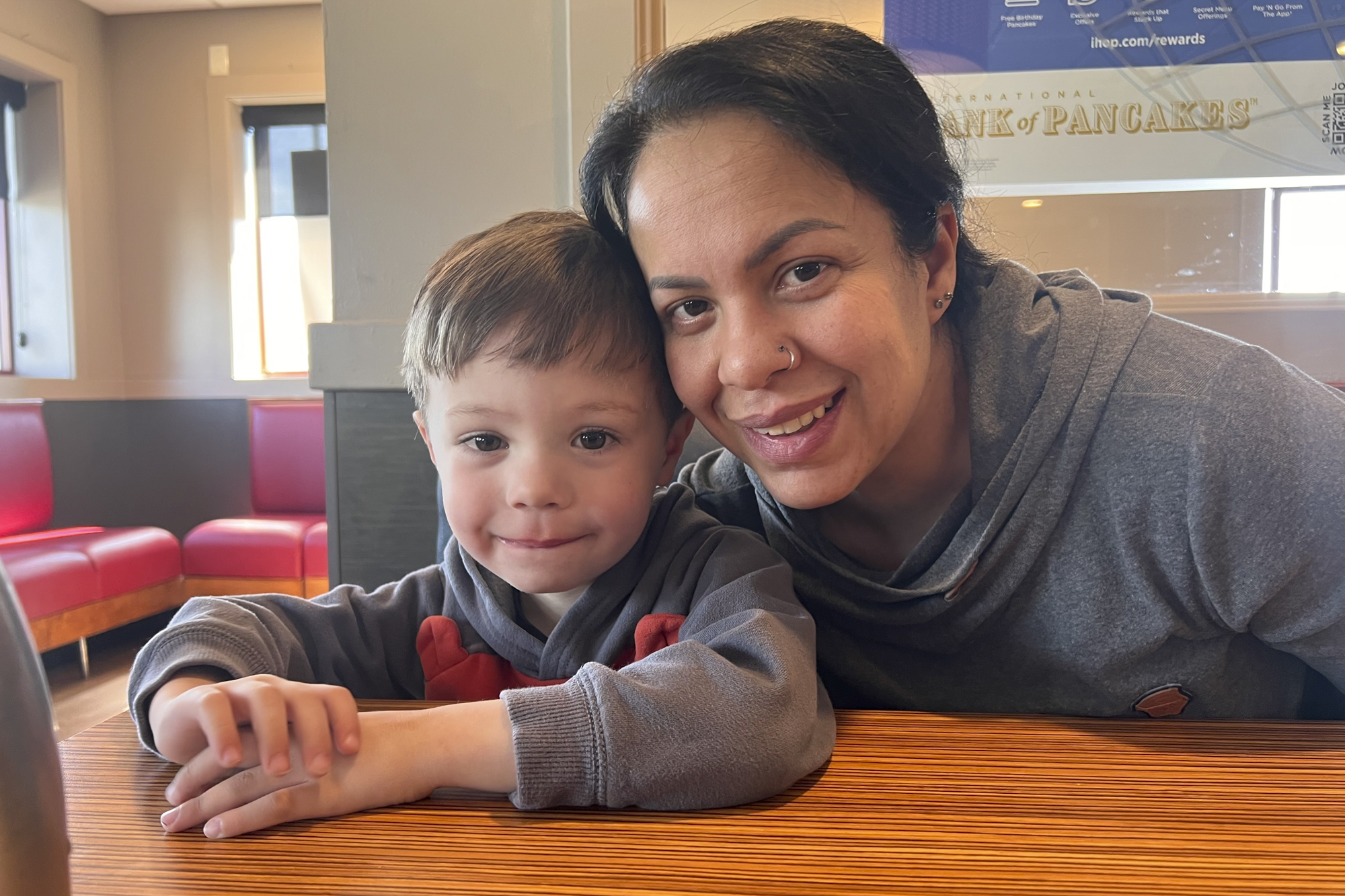 An adult and a child sit together at a table smiling at the camera.