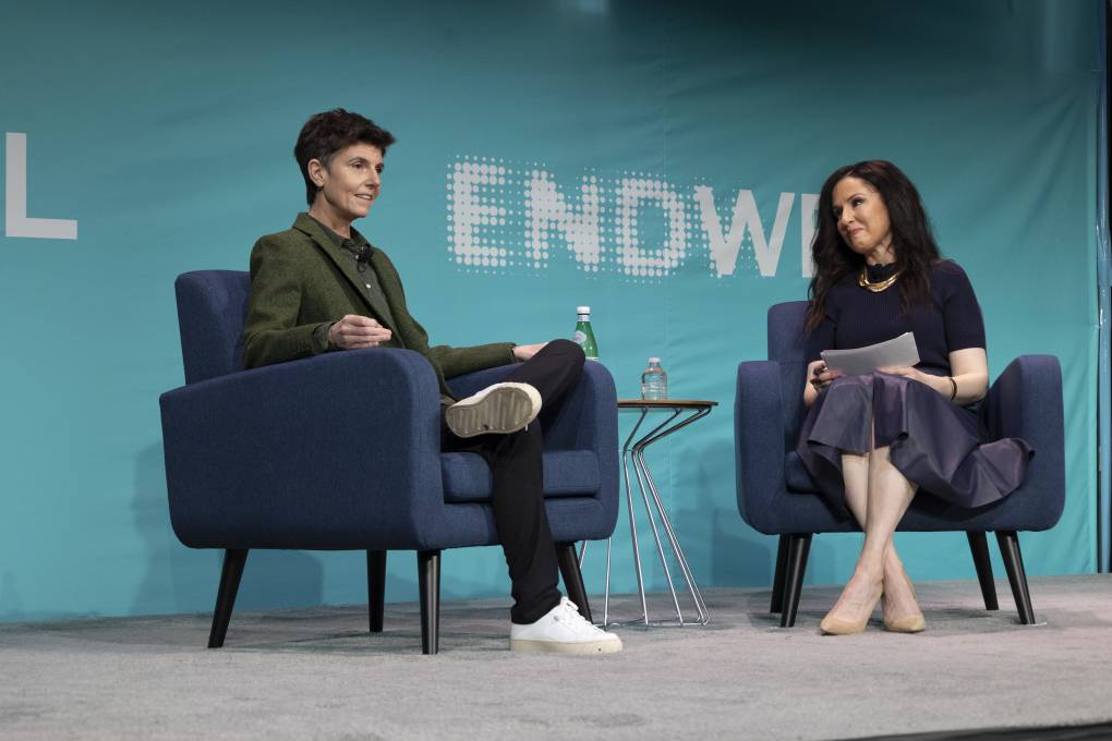 One woman interviews another woman on a stage. On the wall behind them, it says 'Endwell.'