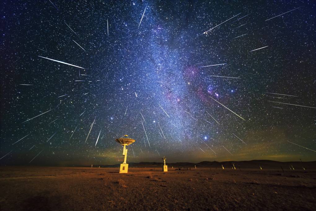 White meteor streaks shoot across a purple-gray night sky.