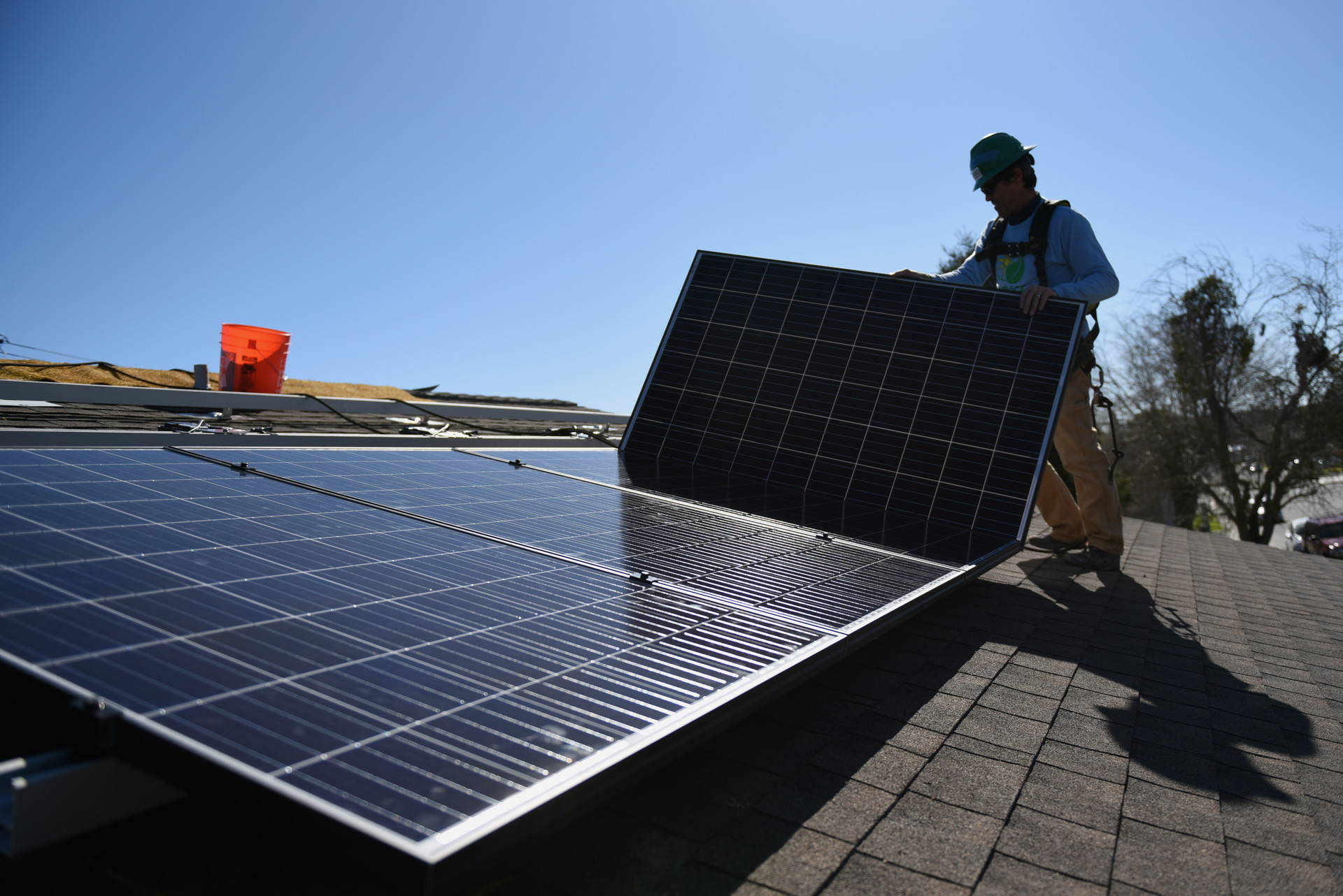 A man in a hard hat installs solar panels on the roof of a house.