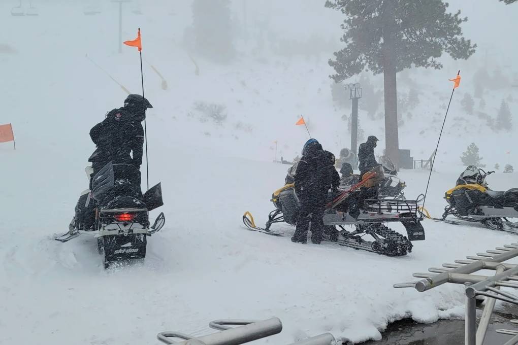 Rescue crews on snowmobiles gather in the snow at the bottom of a mountain.