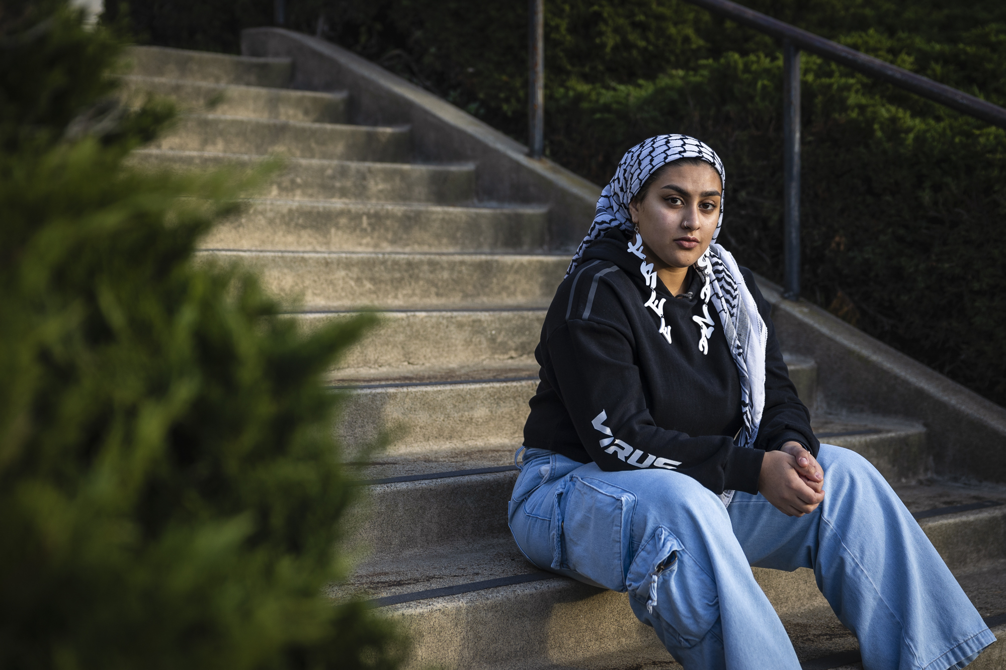 A person wearing a headscarf sits on a set of stairs in an outdoor setting.