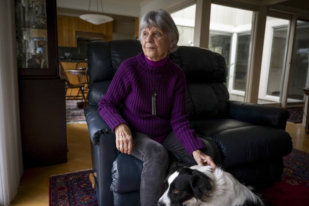 An older woman sits in a leather chair and pets her dog.