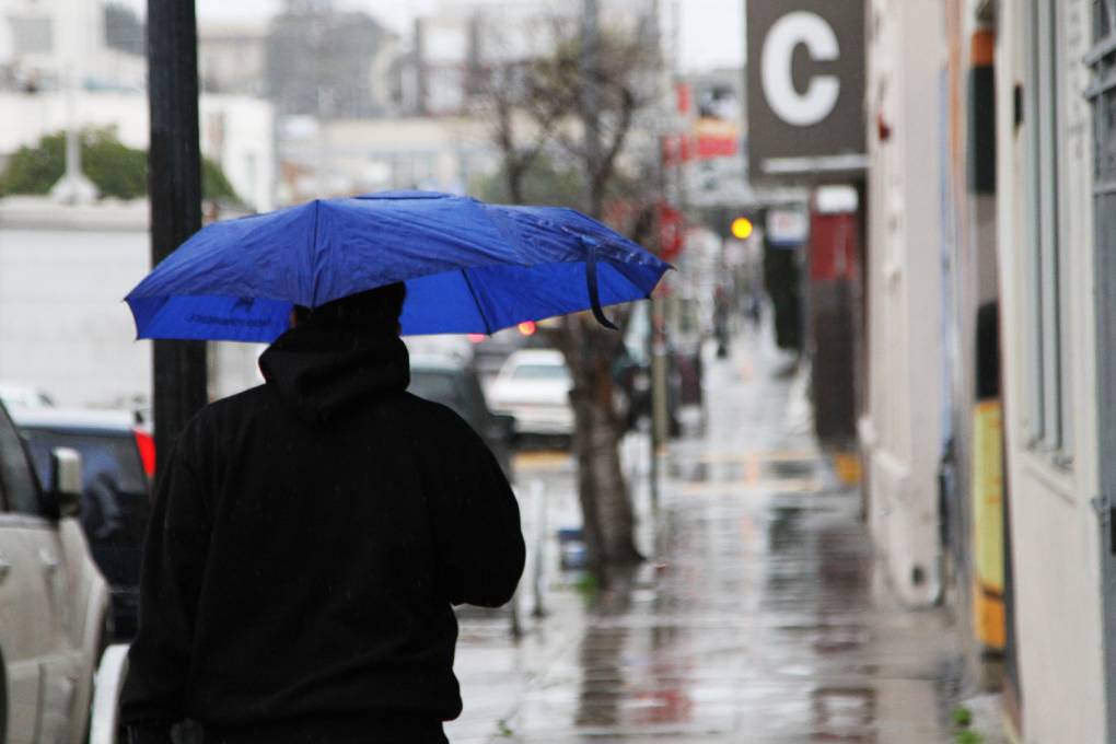 A person holding a blue umbrella on the sidewalk in a city as it rains.