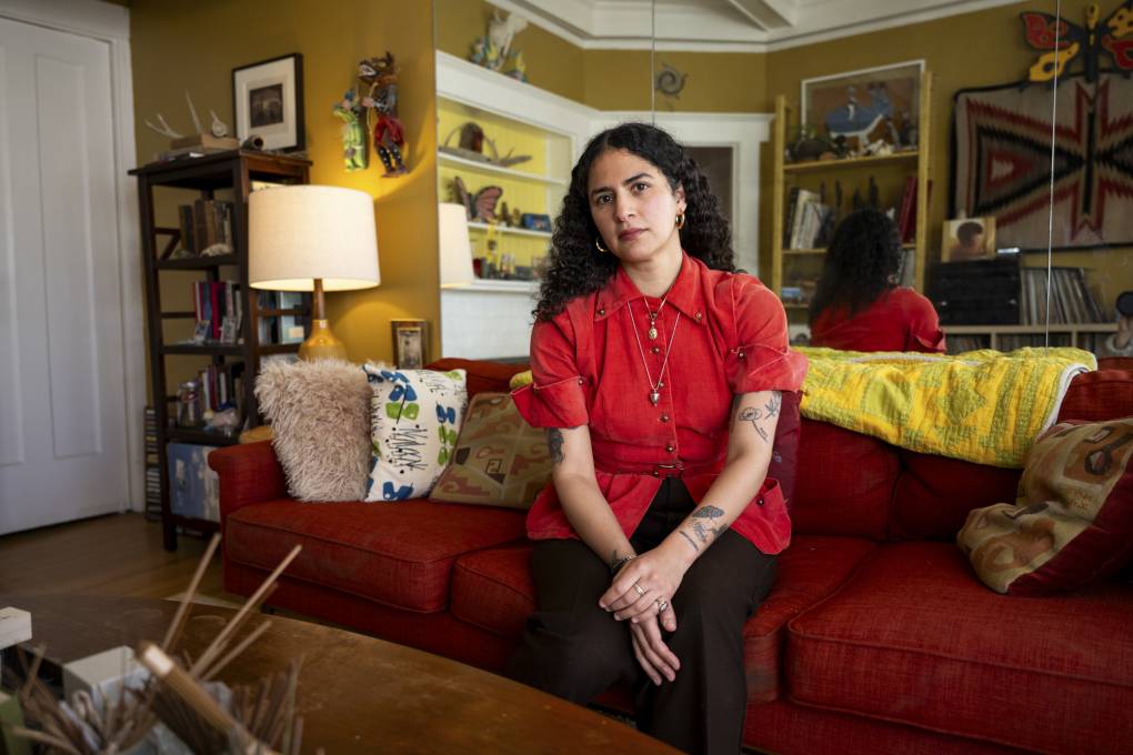 A woman wearing a red shirt sits on a couch in a home.
