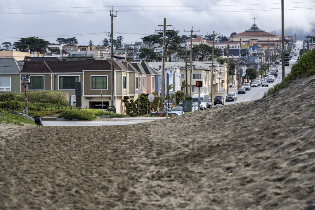 A view of a residential neighborhood with a sandy coastline on the other side of a road.