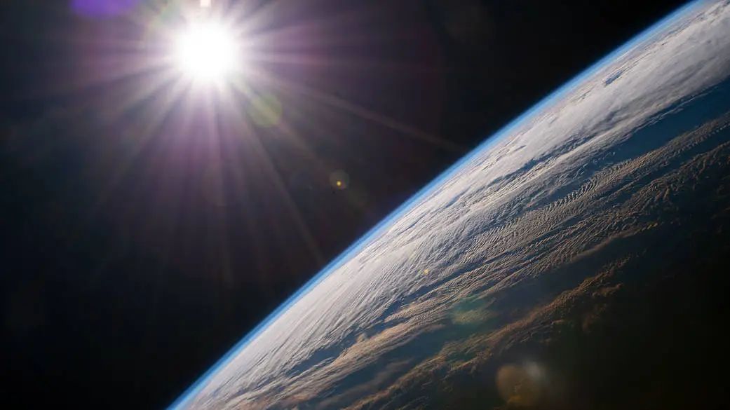 The white sun shines in the distance behind blue Earth.
