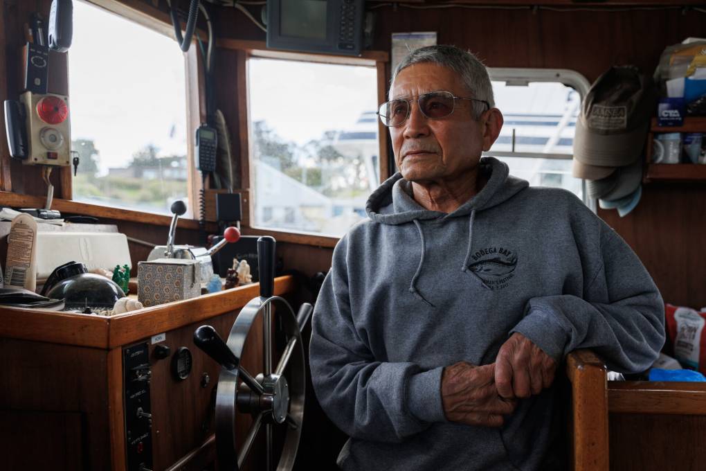 A man wearing a grayish hoodie and sun glasses rests his arm inside a boat.