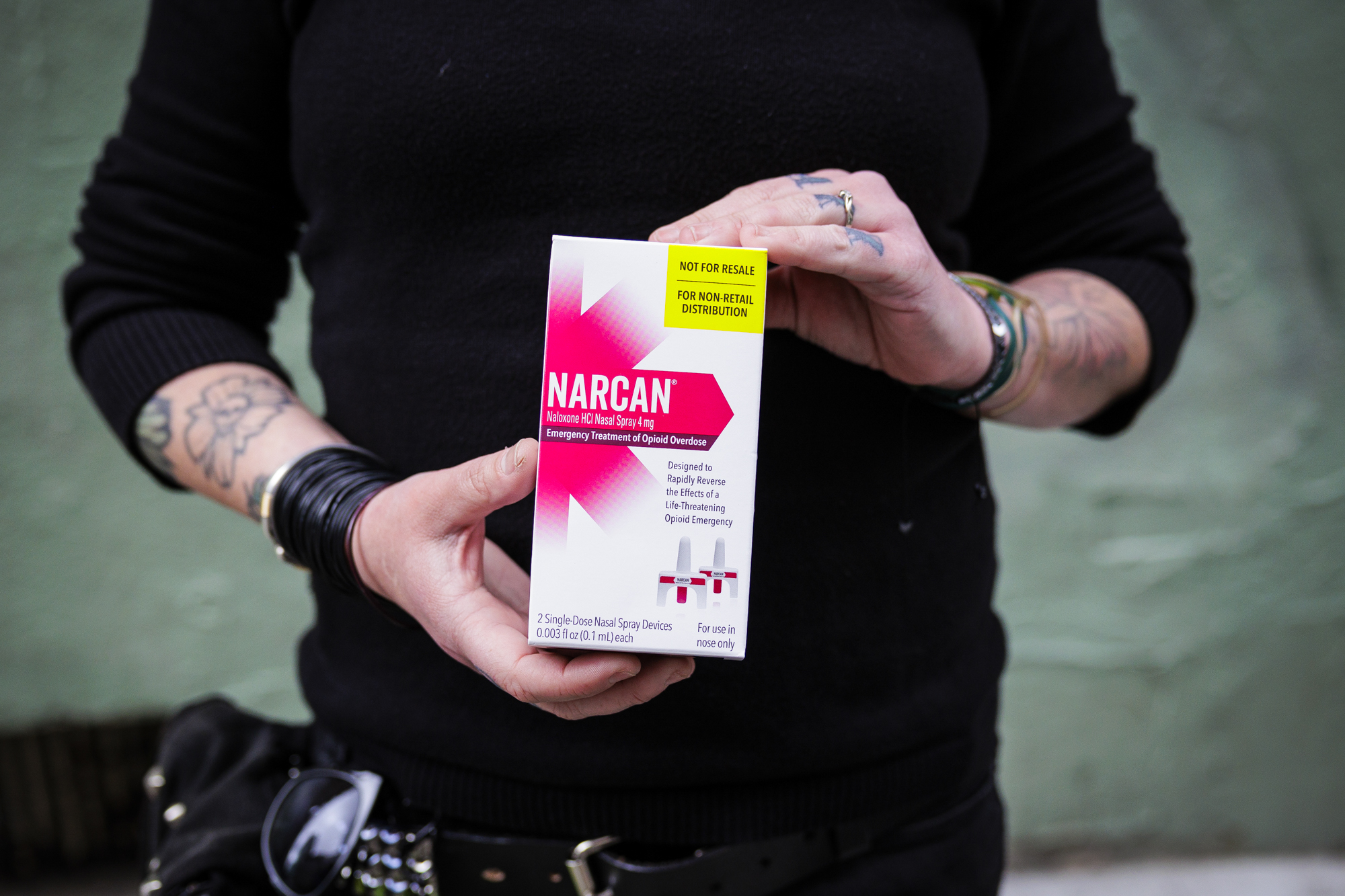 A woman with tattoos holds a box of narcan. 