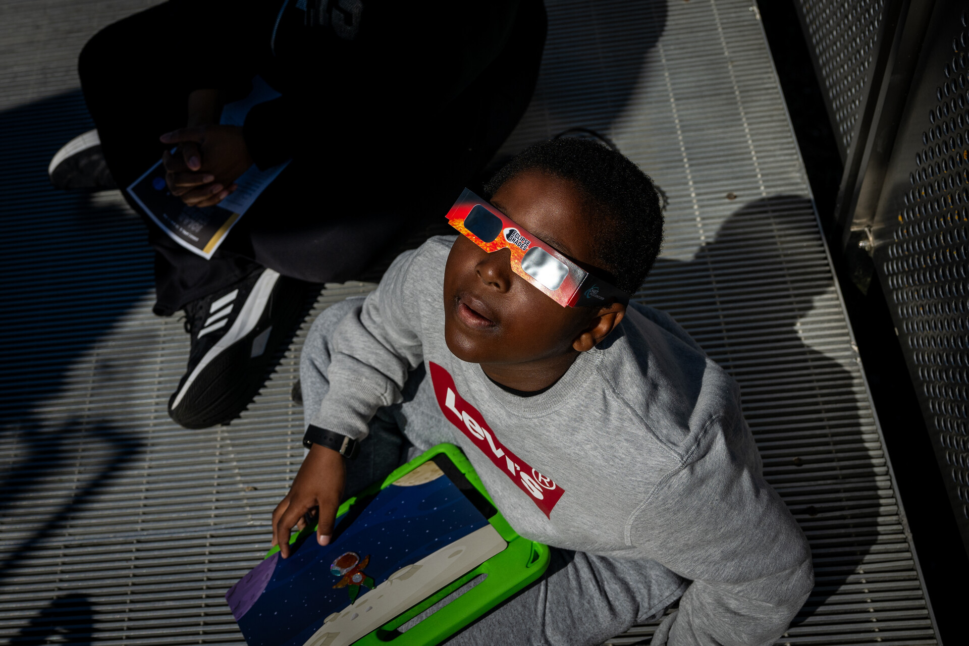 A young girl in eclipse glasses looks up at the sky.