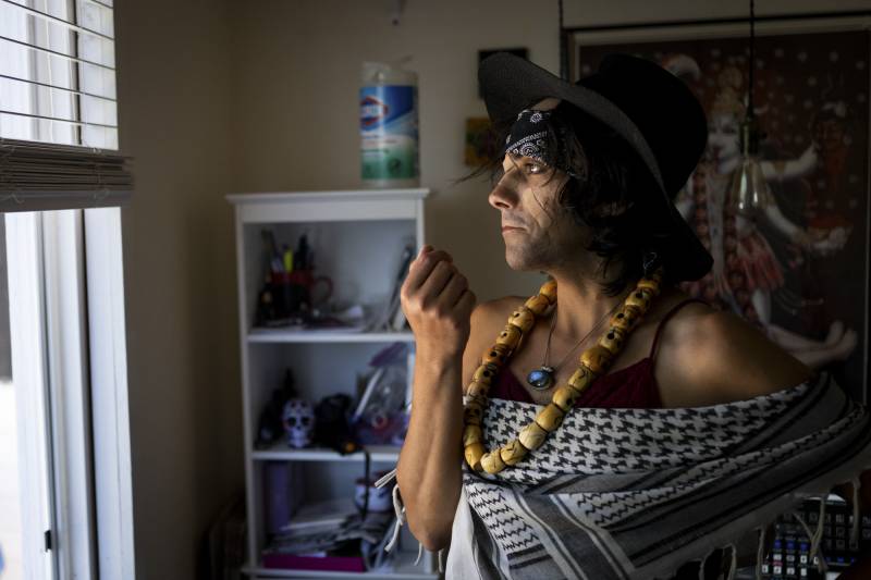 A person wearing a hat and a large necklace inside a house.