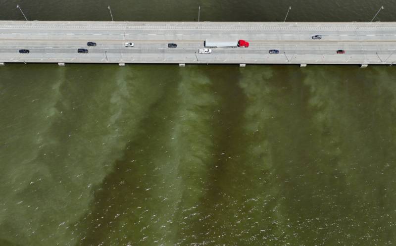 An aerial view of cars driving on a bridge over brownish water.