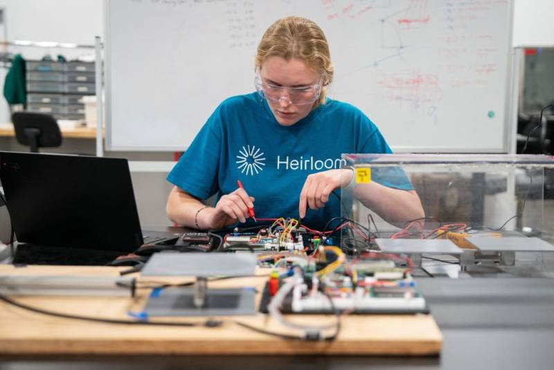 A young white woman uses tools to work on technical instrumentation at a workbench.