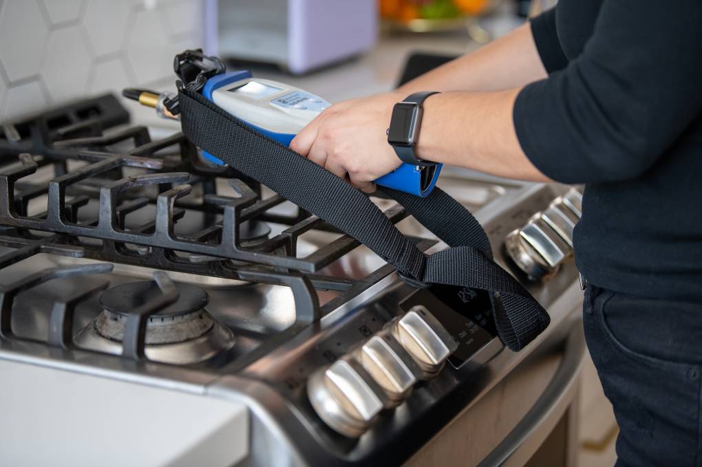 A person holds a small machine near a gas stove.