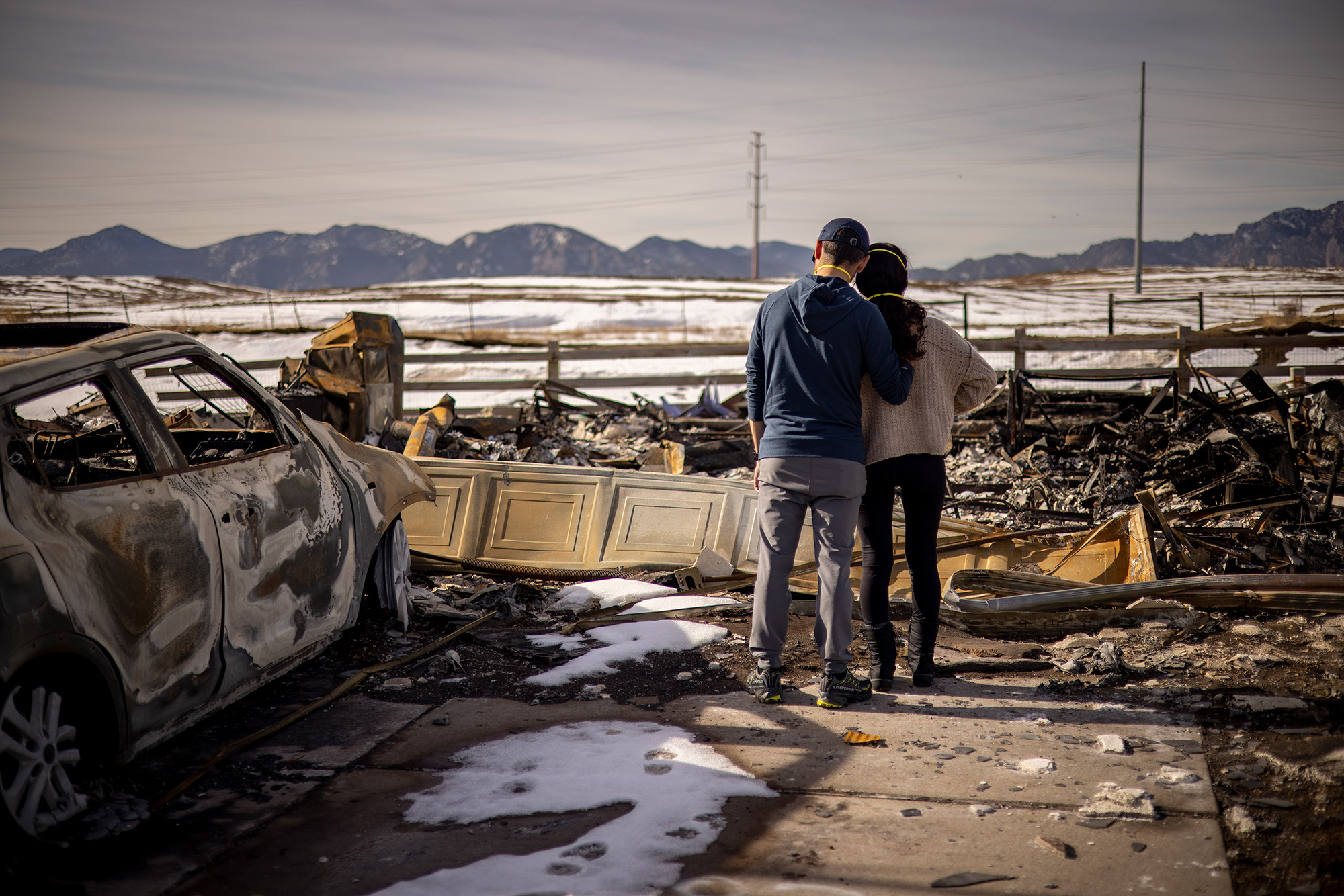 A couple holds each other while looking at a burned-down building.