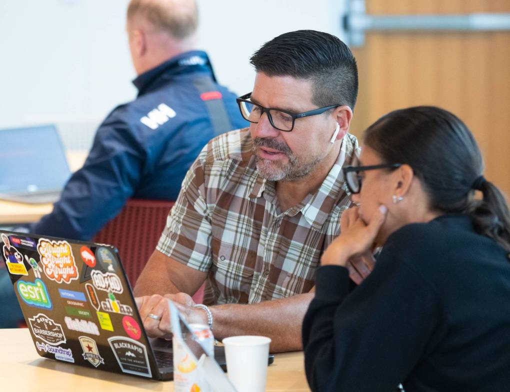 Two educators sit together looking at an open laptop.