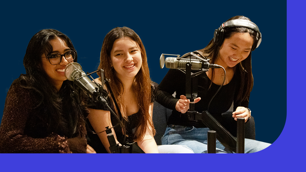 Three students sit around microphones in a recording studio
