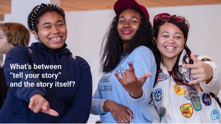 Three smiling students pose together and gesture toward the camera. White text over the image asks, “What’s between ‘tell your story’ and the story itself?”