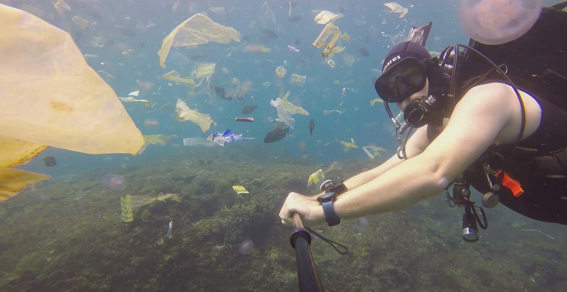 Scuba diver swims amidst plastic debris floating in the ocean