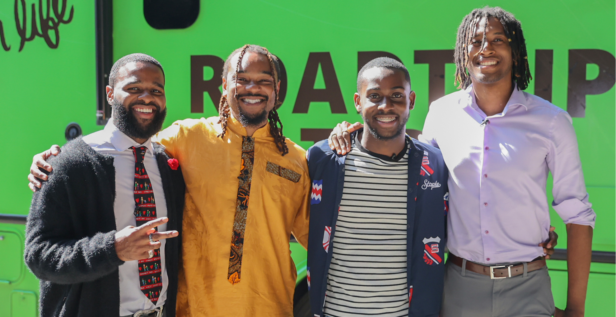 Four Black men pose for the camera in front of the Roadtrip Nation green RV.