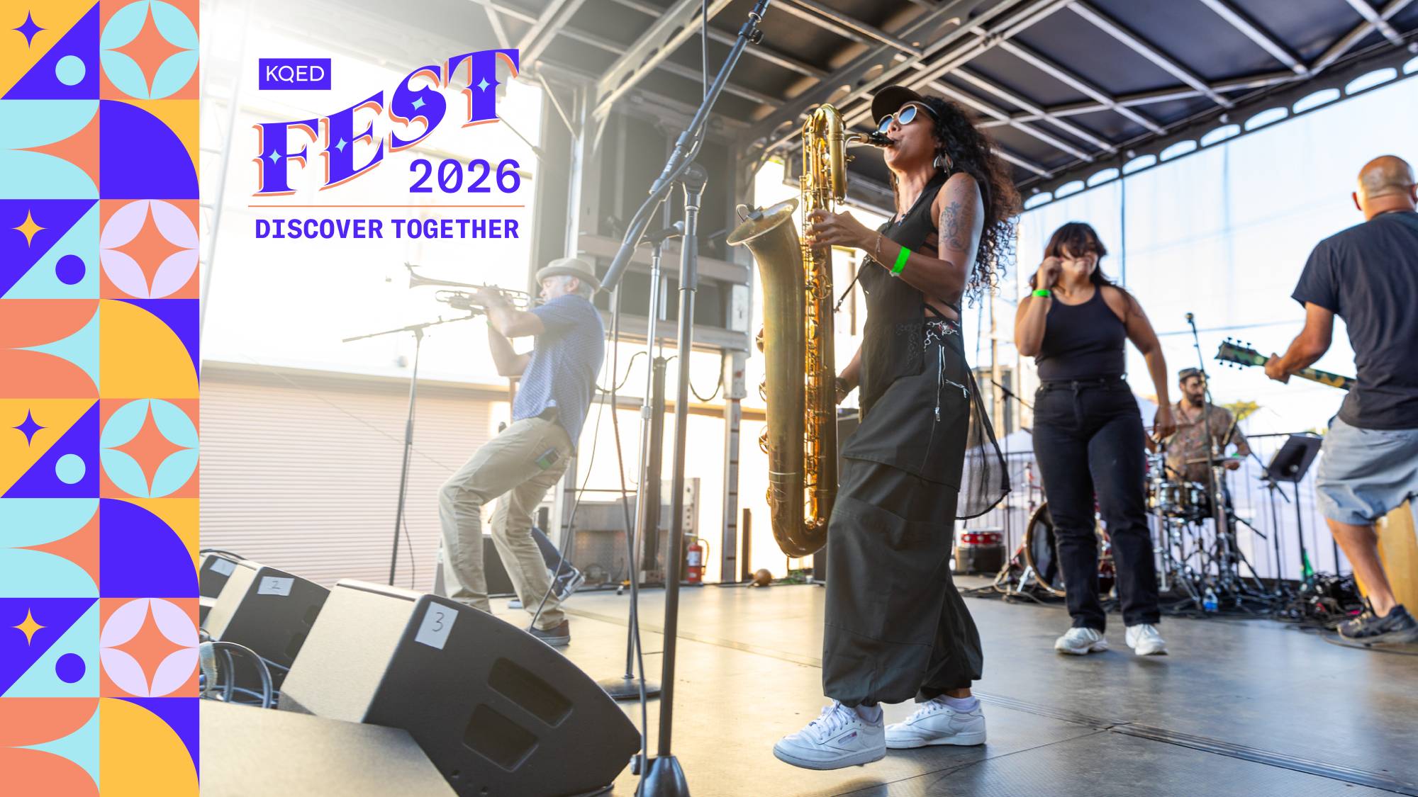 A live music performance on an outdoor stage at a festival. In the foreground, a musician wearing a black outfit and white sneakers plays a large saxophone, standing near a microphone. Behind and around them, other band members perform—one playing trumpet, another singing into a microphone, and a drummer seated at a drum kit. Stage equipment like speakers and mic stands is visible. Bright daylight filters through the open structure of the stage. On the left side of the image, a colorful geometric border frames the scene, alongside text that reads “KQED Fest 2026 – Discover Together.”