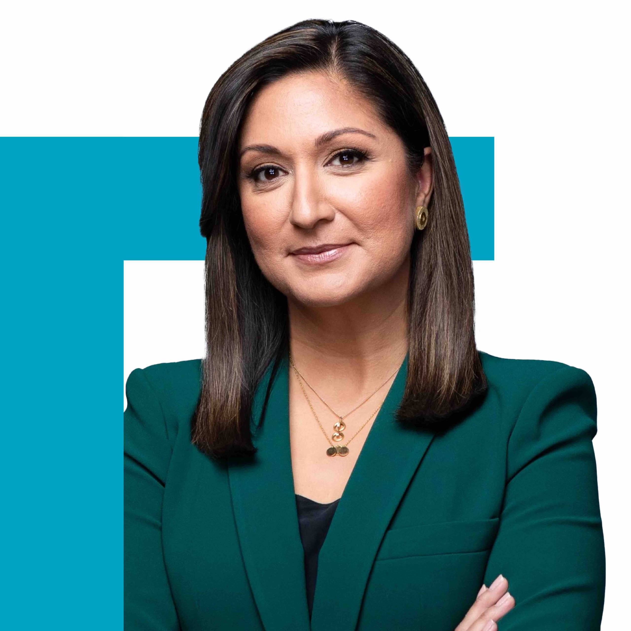 PBS NewsHour co-anchor Amna Nawaz, a woman with dark hair in a green blazer, is framed by a blue right-angle graphic over her upper left shoulder.