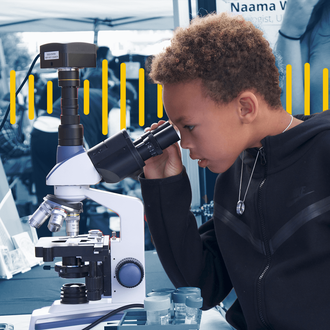 Young boy wearing a silver necklace looks into a microscope