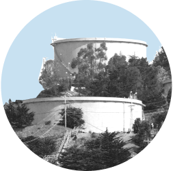 Two refinery drums sit amongst trees in the hills of Contra Costa County. The image is in black and white and contained in a light blue circle.