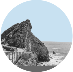 A boardwalk passes by a large rock formation along the Pacific coast in Marin County. The image is in black and white and contained in a light blue circle.
