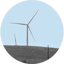 Wind turbines rise above agricultural hills in Solano County. The image is in black and white and contained in a light blue circle.